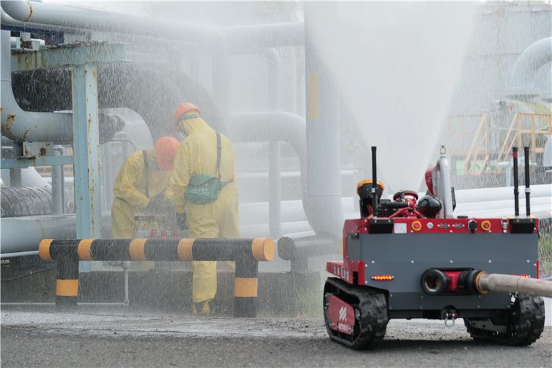 Under the protection of a firefighting robot, leak containment personnel simulate a pipe-clamping operation to stop the leakage.